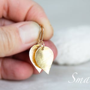 May include: Gold teardrop shaped earrings with a hammered texture. The earrings are small and delicate.
