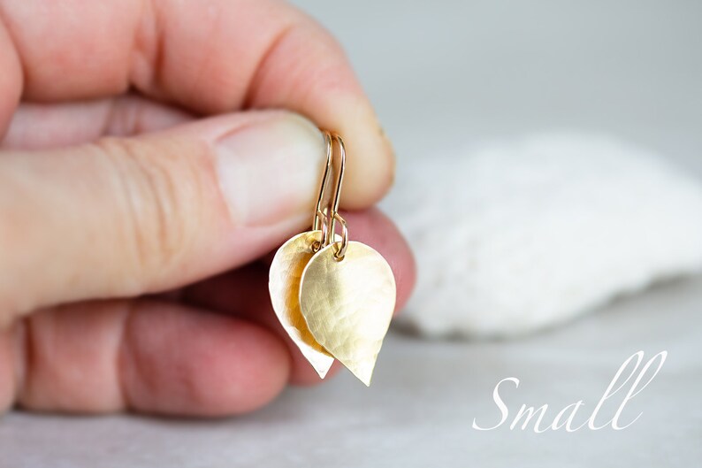 May include: Gold teardrop shaped earrings with a hammered texture. The earrings are small and delicate.