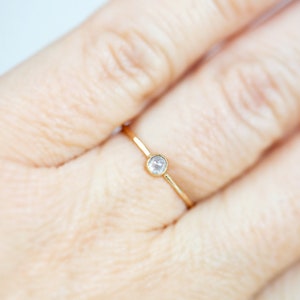 Pode incluir: Um delicado anel de ouro com uma pequena gema redonda e transparente.
