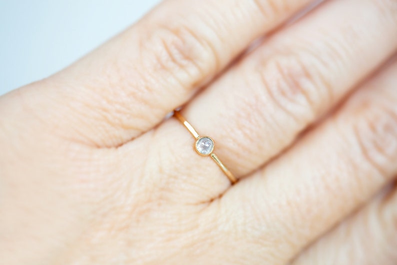 Pode incluir: Um delicado anel de ouro com uma pequena gema redonda e transparente.