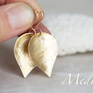 May include: Gold leaf earrings with a hammered texture. The earrings are teardrop shaped and have a medium size.