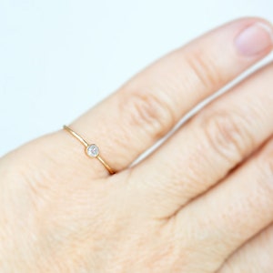 Pode incluir: Um delicado anel de ouro com um &uacute;nico diamante pequeno e redondo.