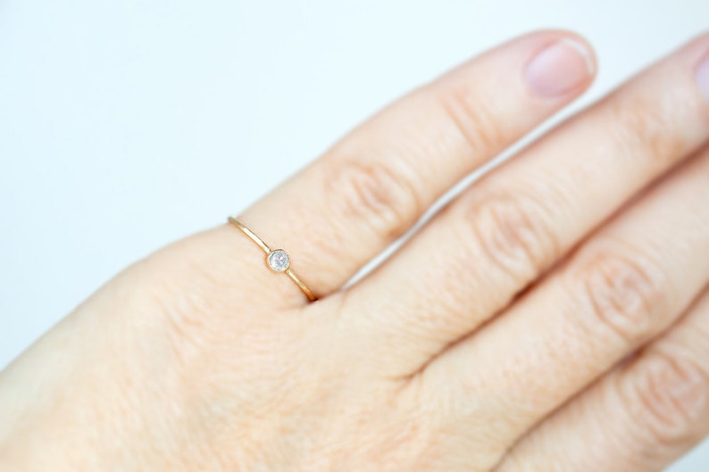 Pode incluir: Um delicado anel de ouro com um &uacute;nico diamante pequeno e redondo.