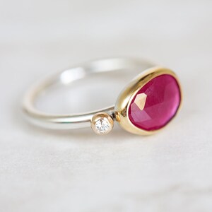 May include: A silver and gold ring with a large, faceted, pink gemstone and a small, round, clear gemstone.