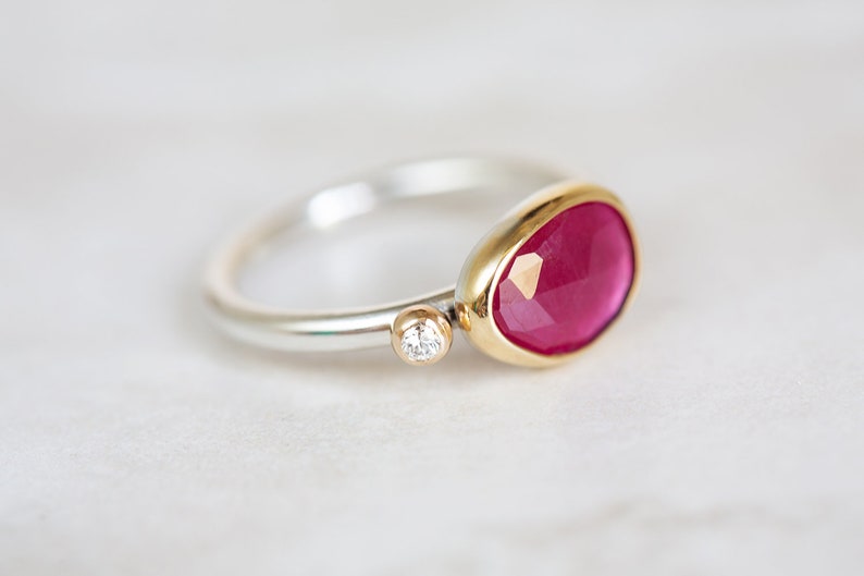 May include: A silver and gold ring with a large, faceted, pink gemstone and a small, round, clear gemstone.