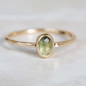 May include: A delicate gold ring with a green oval gemstone set in a bezel setting.