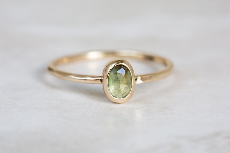 May include: A delicate gold ring with a green oval gemstone set in a bezel setting.