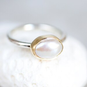 May include: A silver ring with a gold setting and a white pearl.