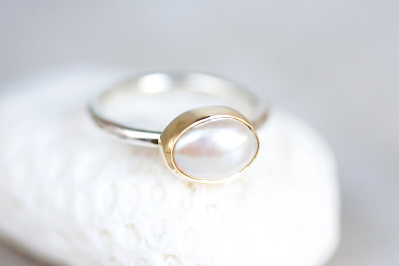May include: A silver ring with a gold setting and a white pearl.