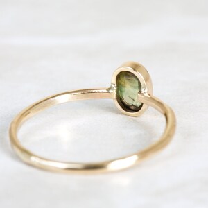 May include: A gold ring with a green oval gemstone set in a bezel setting. The ring is simple and elegant.