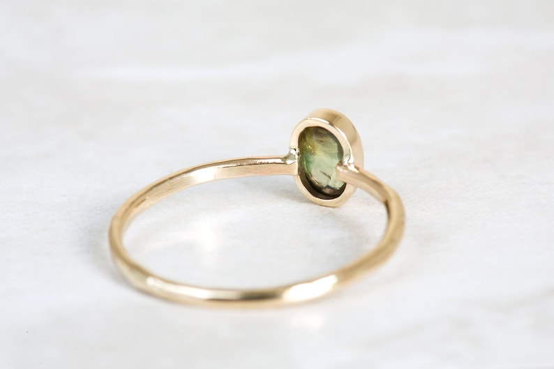May include: A gold ring with a green oval gemstone set in a bezel setting. The ring is simple and elegant.