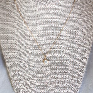 May include: A delicate gold chain necklace with a small, clear gemstone pendant.