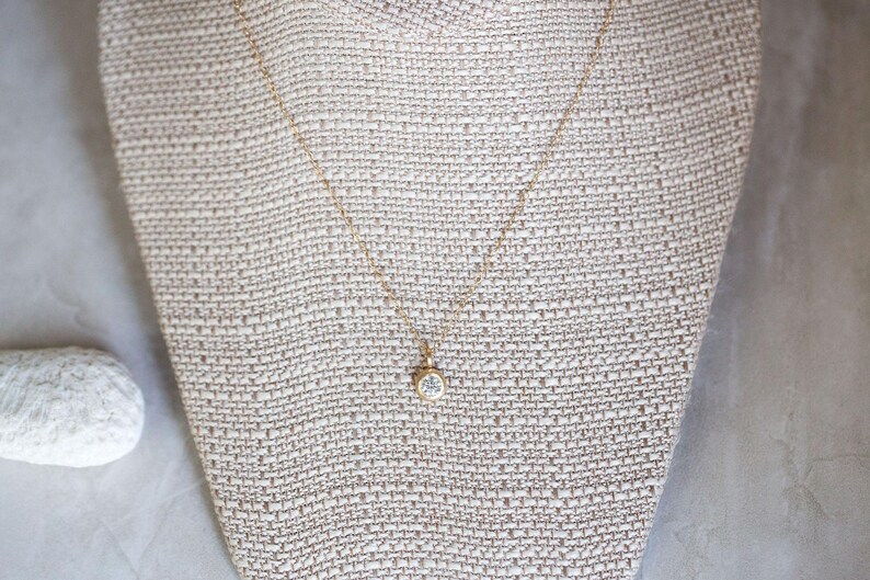 May include: A delicate gold chain necklace with a small, clear gemstone pendant.