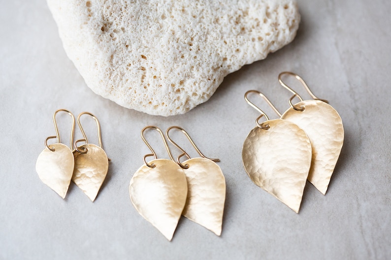 May include: Three pairs of gold leaf-shaped earrings with hammered textures. The earrings are of different sizes.