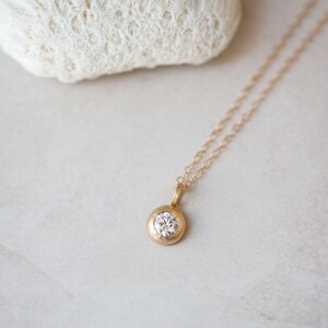 May include: A delicate gold chain necklace with a small round pendant featuring a clear gemstone.