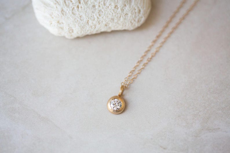 May include: A delicate gold chain necklace with a small round pendant featuring a clear gemstone.