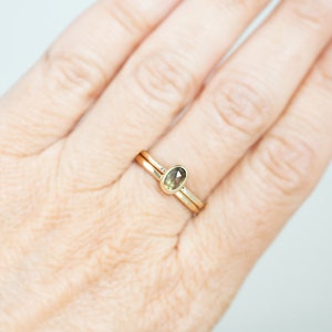 May include: A gold ring with a small, oval-shaped gemstone set in the center. The ring is worn on a finger.