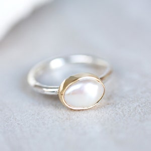 May include: A silver ring with a gold setting and a white pearl.