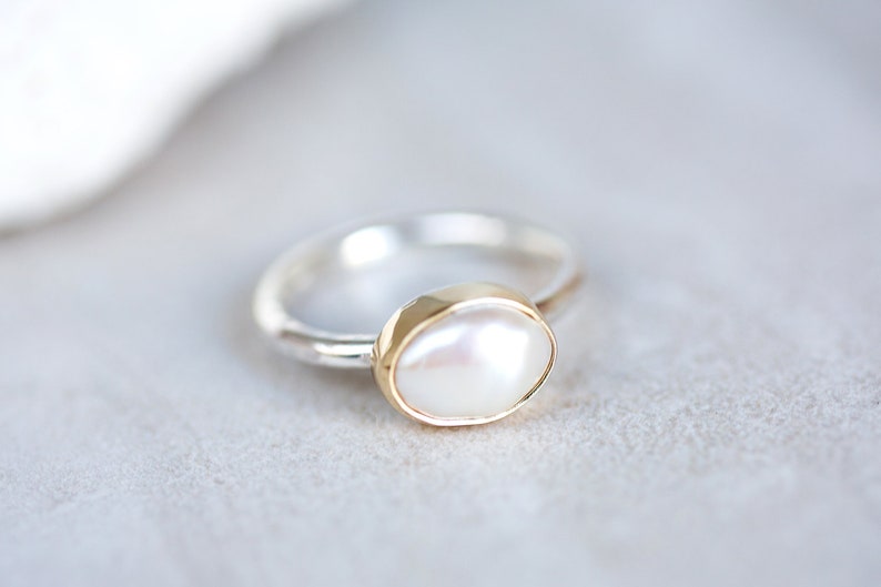 May include: A silver ring with a gold setting and a white pearl.