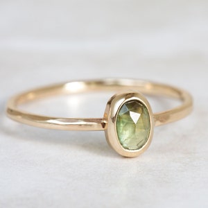 May include: A delicate gold ring with a bezel setting featuring a green gemstone.