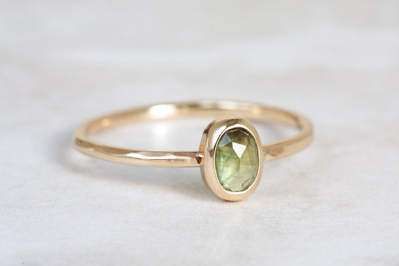 May include: A delicate gold ring with a bezel setting featuring a green gemstone.