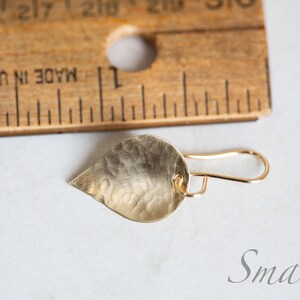 May include: A small, gold-colored, teardrop-shaped earring with a hammered texture. The earring is hanging from a gold hook.