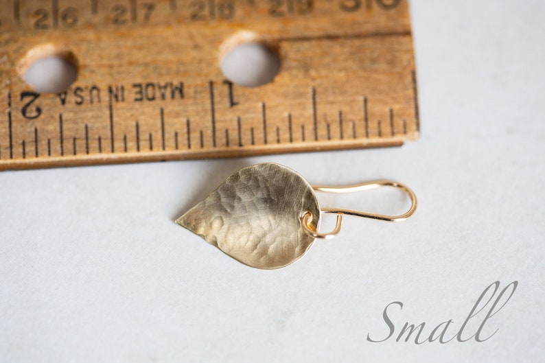 May include: A small, gold-colored, teardrop-shaped earring with a hammered texture. The earring is hanging from a gold hook.