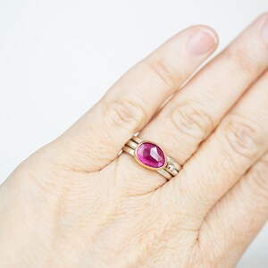 May include: A pink gemstone ring set in gold with a delicate band. The ring is worn on a person's finger.
