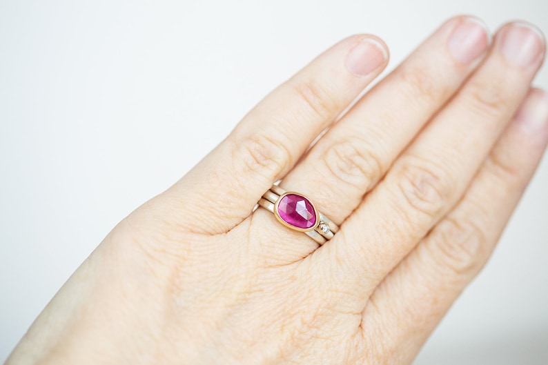 May include: A pink gemstone ring set in gold with a delicate band. The ring is worn on a person's finger.