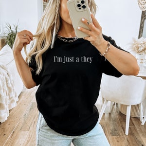 May include: A black t-shirt with the text "I'm just a they" printed in white on the front.