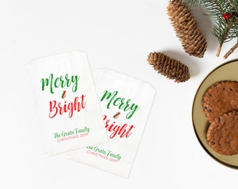 May include: Two white paper gift bags with red and green text that reads "Merry & Bright". The bags are personalized with "The Grain Family Christmas 2019".