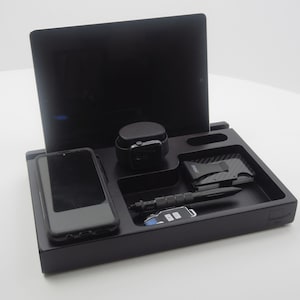 May include: A black wooden desk tidy with sections for a tablet, smartphone, smartwatch, wallet, pen, and keys. The organiser has a minimalist design and a matte finish. The text "STANDVAST" is visible on the lower right corner.