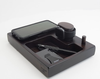 May include: A dark wood valet tray with compartments for a phone, watch, pen, and wallet. The tray has a black finish and the text "STANDFAST WOOD" is engraved on the bottom.