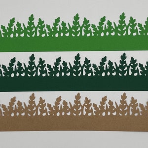 May include: Three strips of paper cut in the shape of grass. The top strip is green, the middle strip is dark green, and the bottom strip is tan. The grass blades are detailed and create a decorative border.