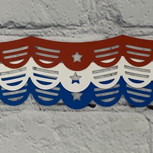 May include: A patriotic paper banner in red, white, and blue. The banner features a scalloped edge design with stars and stripes cutouts. The colors are arranged in horizontal stripes, evoking a sense of national pride.