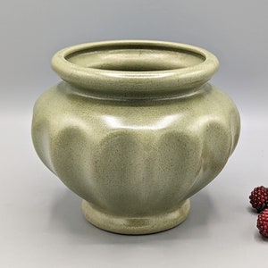 Op de afbeelding: Een kleine, groene keramische pot met een geribbeld ontwerp. De pot heeft een gladde, glanzende afwerking en een ronde basis.