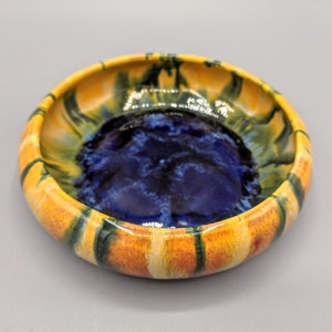 Può includere: Un piccolo piatto rotondo in ceramica con una glassa blu all'interno e una glassa gialla, arancione e verde all'esterno.