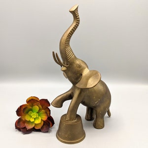 May include: A gold brass elephant figurine with its trunk raised in the air. The elephant is standing on a round base.