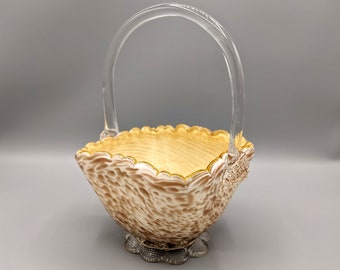 May include: A glass basket with a clear handle and a textured, brown and gold design. The basket has a scalloped rim and a gold trim.