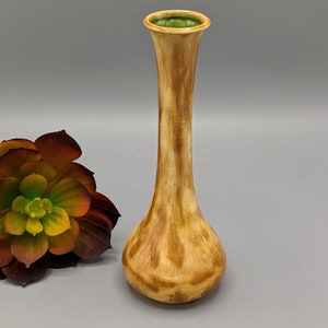 Op de afbeelding: Een kleine, keramische vaas met een bruine en gele glazuur. De vaas heeft een smalle hals en een brede, afgeronde basis. De bovenkant van de vaas is geglazuurd in een lichtgroene kleur.