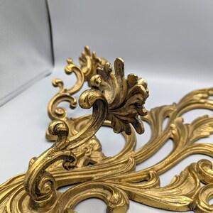 May include: A pair of gold-coloured, ornate wall decorations with a scrolling, floral design. The decorative pieces feature detailed leaf and vine patterns, creating an elegant, vintage aesthetic. The metalwork has a slightly aged appearance, adding to its antique charm.