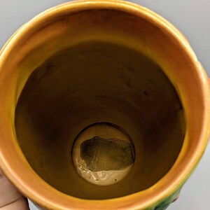 Może przedstawiać: Brązowy ceramiczny wazon z zielonym i ż&oacute;łtym wzorem kwiatowym. Wazon ma dwa uchwyty i szeroki otw&oacute;r. Wnętrze wazonu jest widoczne i wydaje się być szkliwione.