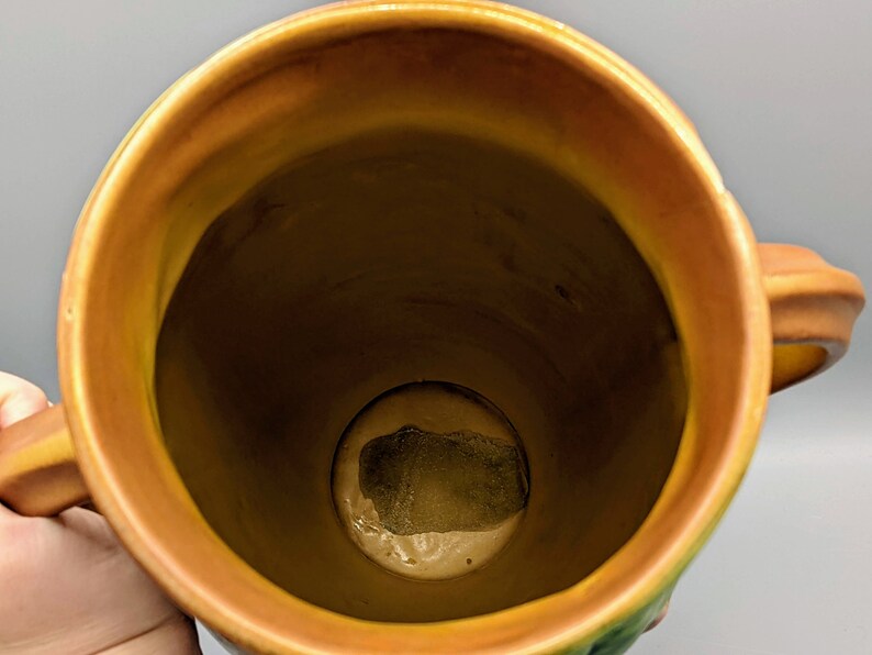 Może przedstawiać: Brązowy ceramiczny wazon z zielonym i ż&oacute;łtym wzorem kwiatowym. Wazon ma dwa uchwyty i szeroki otw&oacute;r. Wnętrze wazonu jest widoczne i wydaje się być szkliwione.