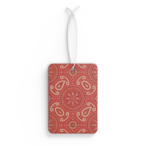 May include: Rectangular air freshener with a red paisley pattern. The design features floral and paisley motifs in shades of red, beige, and brown. A white string is attached for hanging. The air freshener is a decorative item.