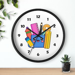 May include: A round wall clock with a black frame and a white face featuring black numbers from 1 to 12. The center displays a colorful illustration of a blue pencil holder with a smiling face, surrounded by various school supplies like pencils.