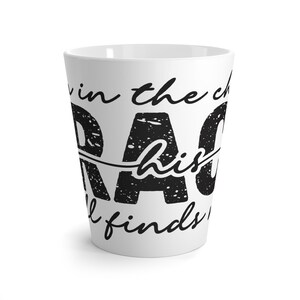 Może przedstawiać: Biały ceramiczny kubek do latte z napisem "DAD" dużymi, czarnymi literami. Kubek zawiera również tekst "in the church his soul finds rest" w czcionce skryptowej. Kubek ma wysoki, zwężający się kształt.