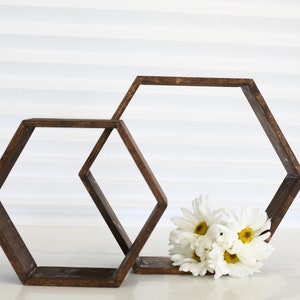 May include: Two wooden hexagonal shelves, one smaller than the other, are stacked on top of each other. A bouquet of white daisies with yellow centers is resting on the bottom shelf.
