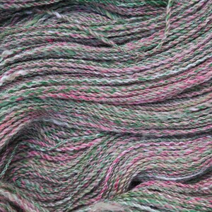 May include: A close-up of a skein of yarn in shades of green, pink, and white. The yarn is soft and fluffy, and it is perfect for knitting or crocheting.