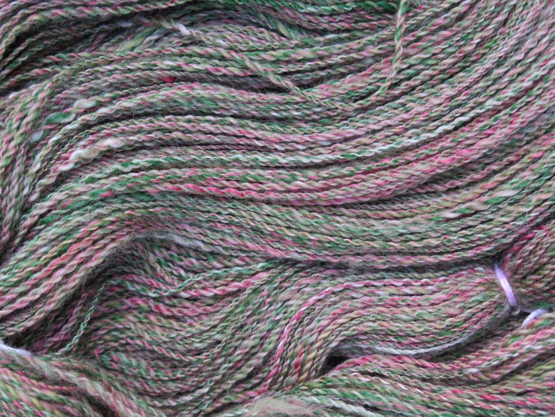 May include: A close-up of a skein of yarn in shades of green, pink, and white. The yarn is soft and fluffy, and it is perfect for knitting or crocheting.