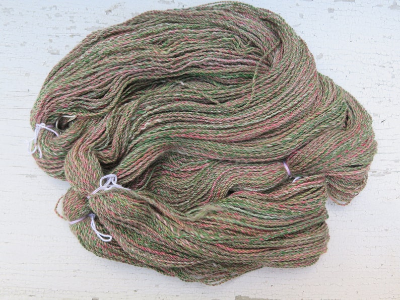 May include: A skein of yarn in shades of green, pink, and white. The yarn is made of natural fibers and has a soft, fuzzy texture.